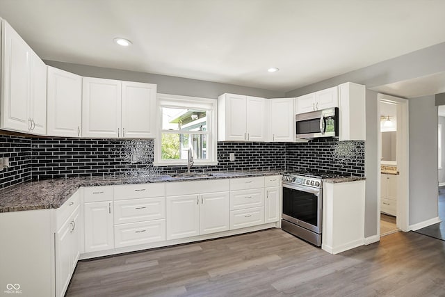 kitchen with appliances with stainless steel finishes, a sink, light wood-style floors, dark stone counters, and white cabinetry