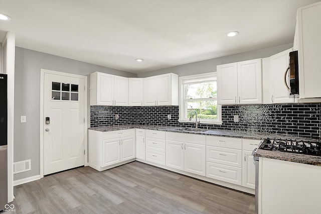 kitchen featuring visible vents, tasteful backsplash, light wood-type flooring, a sink, and stainless steel microwave