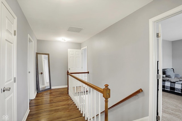 corridor with baseboards, visible vents, wood finished floors, and an upstairs landing