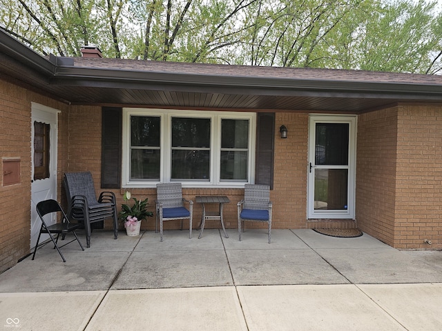 property entrance with a shingled roof, covered porch, a chimney, and brick siding