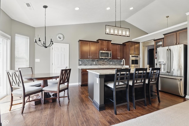 kitchen with appliances with stainless steel finishes, a kitchen island with sink, high vaulted ceiling, a chandelier, and decorative backsplash