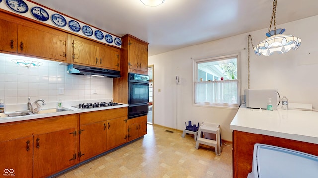 kitchen featuring oven, a sink, gas stovetop, under cabinet range hood, and a warming drawer