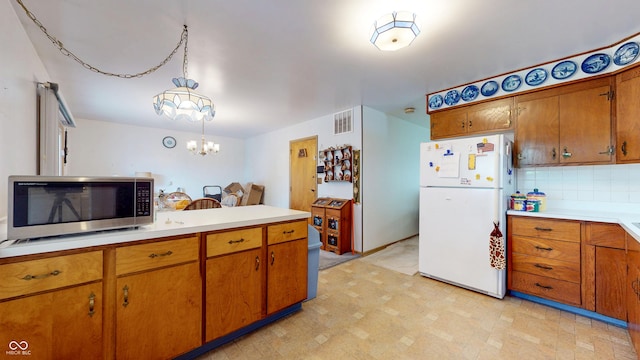 kitchen with visible vents, freestanding refrigerator, brown cabinetry, light countertops, and stainless steel microwave