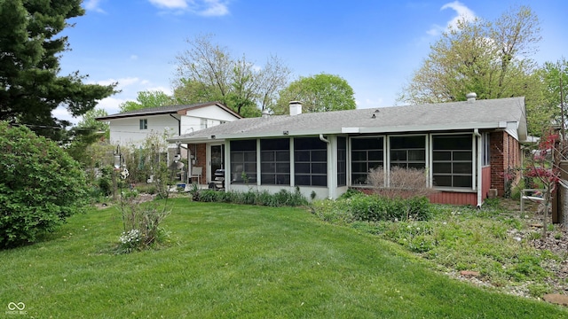rear view of property with roof with shingles, brick siding, a sunroom, a chimney, and a lawn