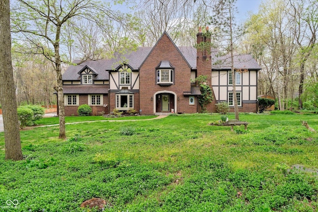 english style home featuring a chimney, brick siding, and a front yard