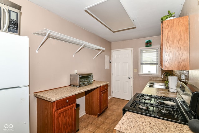 kitchen featuring freestanding refrigerator, a toaster, light countertops, range with gas cooktop, and a sink