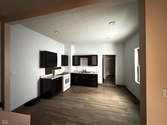 kitchen with white gas stove, dark wood-type flooring, light countertops, dark cabinetry, and a sink