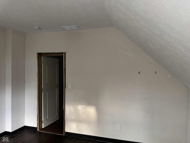 additional living space with dark wood-style flooring, a textured ceiling, visible vents, baseboards, and lofted ceiling