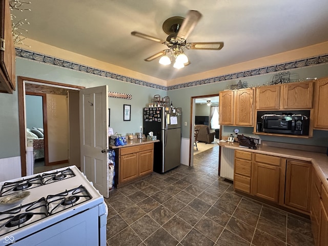 kitchen with ceiling fan, black microwave, light countertops, freestanding refrigerator, and white range with gas stovetop