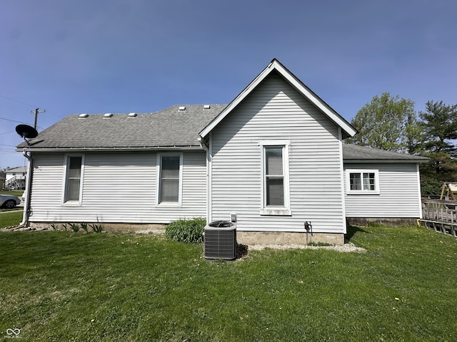 rear view of house featuring a lawn, a shingled roof, and cooling unit
