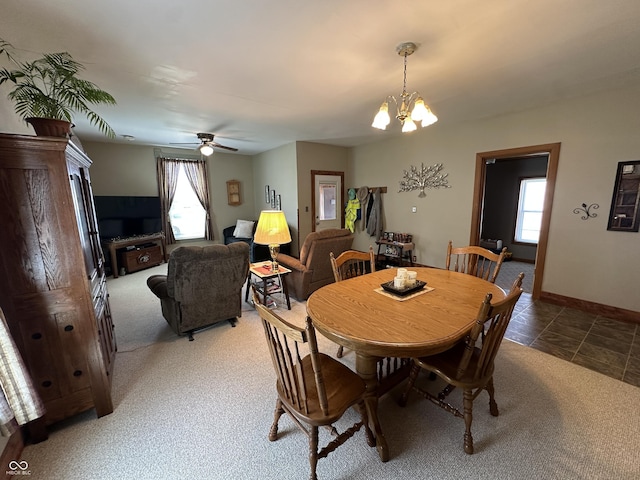 carpeted dining space featuring baseboards, a healthy amount of sunlight, and ceiling fan with notable chandelier