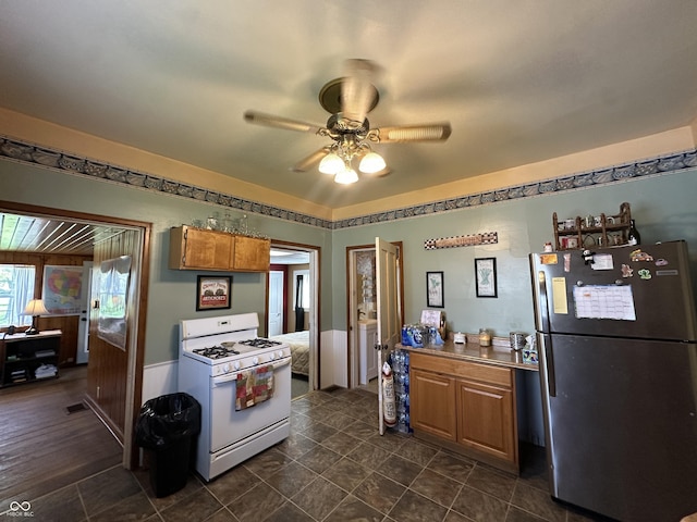 kitchen featuring brown cabinetry, freestanding refrigerator, visible vents, ceiling fan, and white gas range