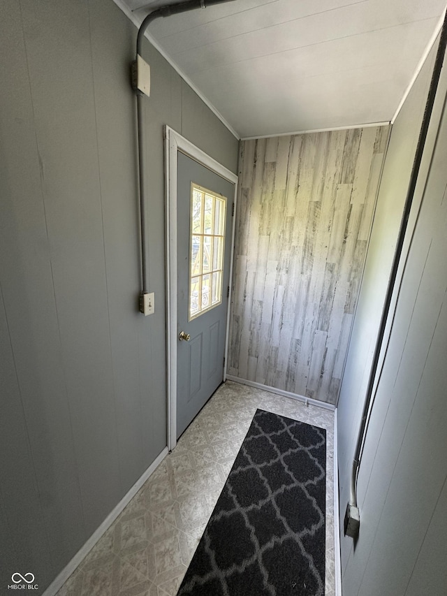 doorway to outside with tile patterned floors, wood walls, and ornamental molding