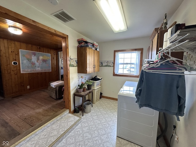 laundry area featuring cabinet space, wood walls, baseboards, light floors, and visible vents