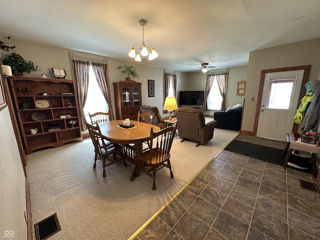 dining area with stone finish floor, plenty of natural light, ceiling fan with notable chandelier, and visible vents