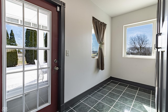 doorway to outside featuring dark tile patterned flooring, baseboards, and a healthy amount of sunlight