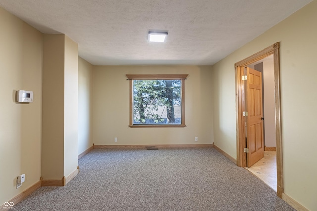 carpeted spare room featuring a textured ceiling and baseboards