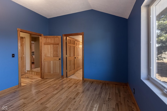 unfurnished bedroom with baseboards, wood finished floors, and lofted ceiling