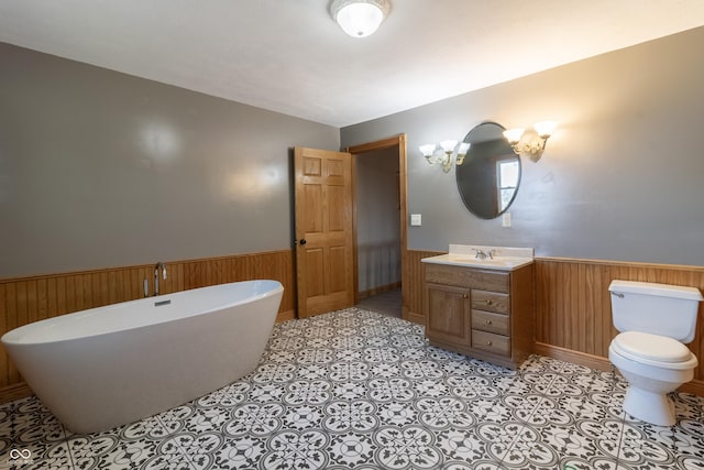 bathroom featuring wainscoting, vanity, toilet, wood walls, and a soaking tub