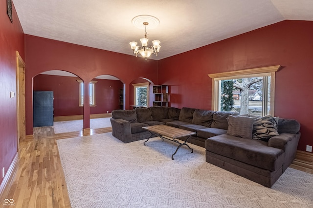 living area featuring an inviting chandelier, arched walkways, light wood-style floors, and a healthy amount of sunlight