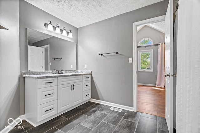 bathroom featuring wood tiled floor, a textured ceiling, vanity, baseboards, and lofted ceiling
