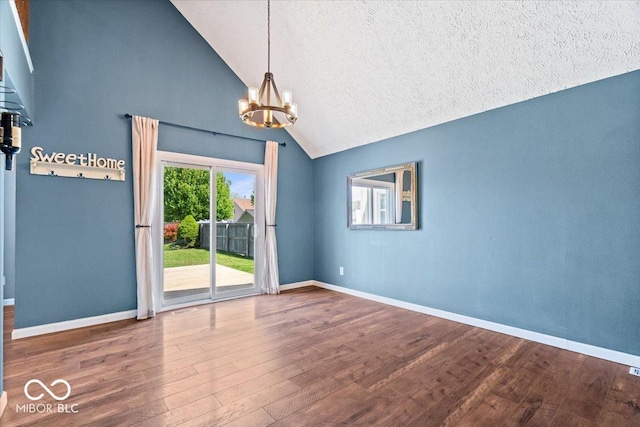empty room featuring a textured ceiling, an inviting chandelier, wood finished floors, and lofted ceiling
