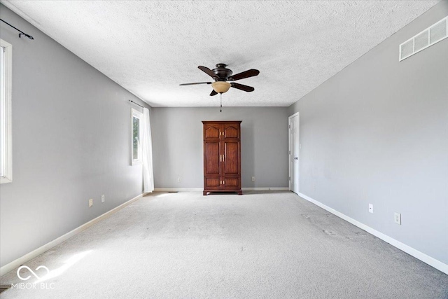 empty room featuring a ceiling fan, a textured ceiling, visible vents, and light colored carpet