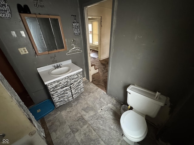 bathroom with toilet, stone finish flooring, and vanity