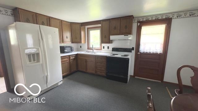 kitchen featuring a sink, white appliances, light countertops, brown cabinetry, and under cabinet range hood