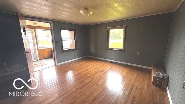 empty room featuring crown molding, baseboards, and wood finished floors
