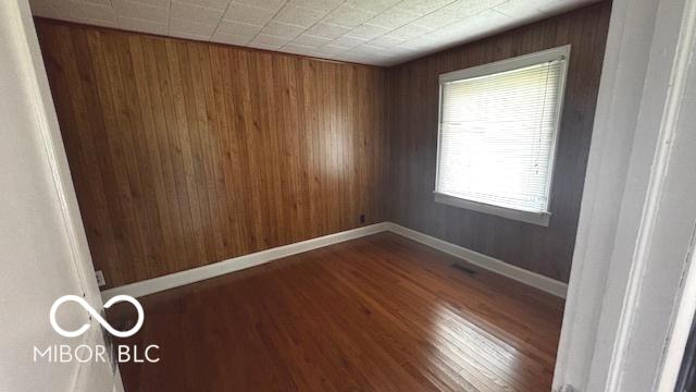 spare room featuring wooden walls, baseboards, and wood finished floors