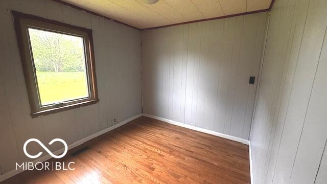 unfurnished room with baseboards, wood walls, and wood finished floors