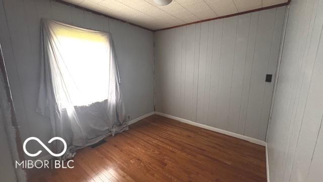 unfurnished room featuring wooden walls, baseboards, and wood finished floors