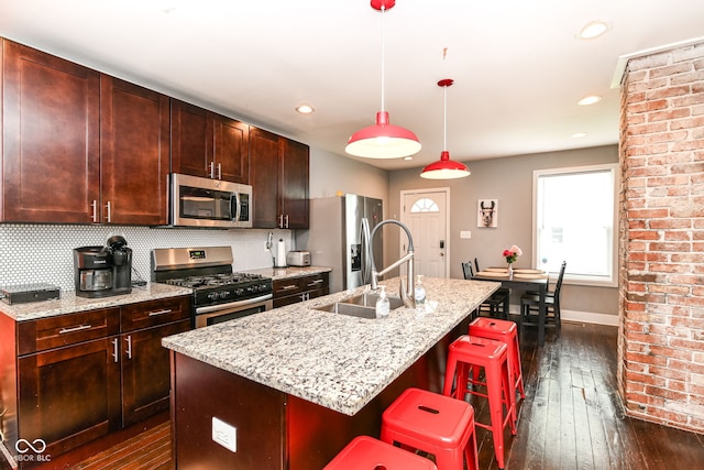 319 S Randolph St, Indianapolis, IN 46201 - kitchen featuring a breakfast bar area, dark wood-style flooring, appliances with stainless steel finishes, light stone countertops, and a center island with sink