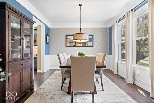 dining room featuring ornamental molding, dark wood-style flooring, wainscoting, a decorative wall, and wallpapered walls