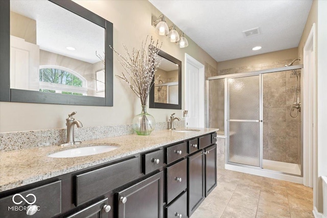 full bathroom featuring double vanity, visible vents, a shower stall, and a sink