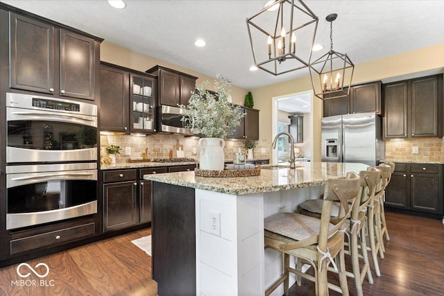 kitchen with dark wood finished floors, appliances with stainless steel finishes, dark brown cabinets, and tasteful backsplash