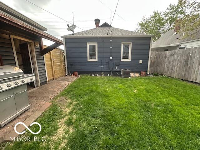 back of property with a lawn, central AC unit, and fence