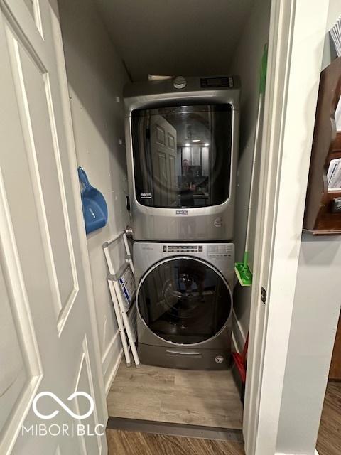 laundry area with stacked washer / drying machine, wood finished floors, and laundry area