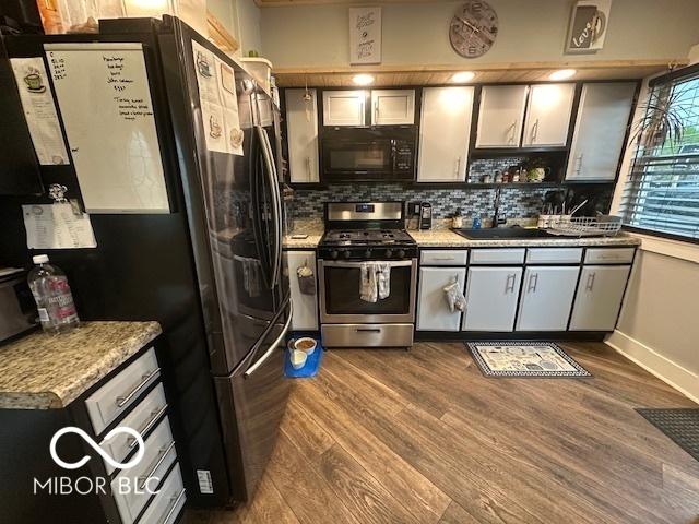 kitchen with baseboards, dark wood-type flooring, a sink, backsplash, and stainless steel appliances