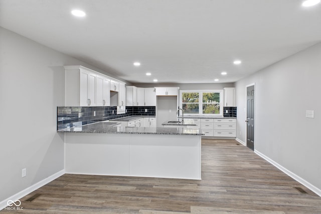 kitchen with stone counters, a peninsula, backsplash, and white cabinetry