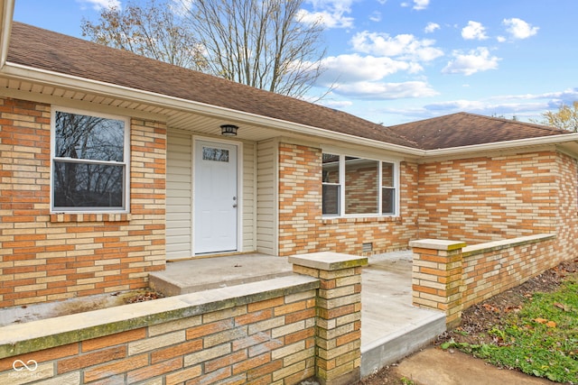 entrance to property with a shingled roof and brick siding