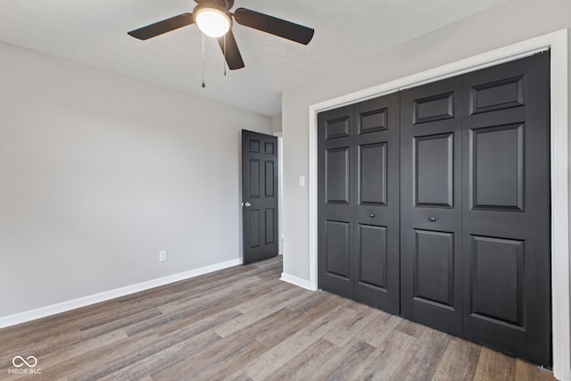 unfurnished bedroom featuring a closet, a ceiling fan, baseboards, and wood finished floors