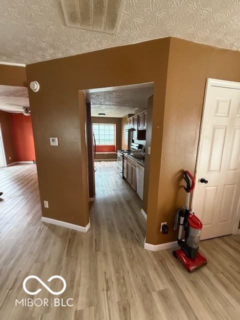 corridor featuring baseboards, a textured ceiling, visible vents, and wood finished floors