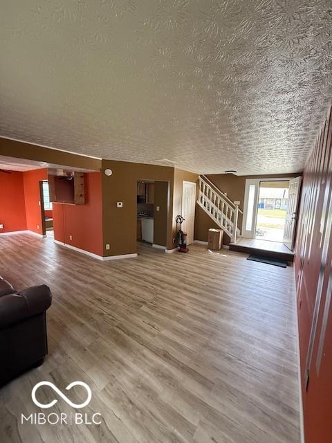 unfurnished living room with baseboards, a textured ceiling, wood finished floors, and stairway