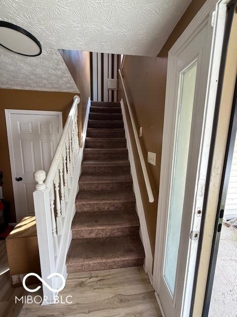 stairway with a textured ceiling and wood finished floors