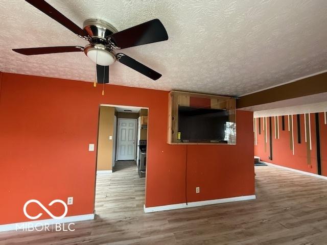 unfurnished living room featuring a ceiling fan, a textured ceiling, baseboards, and wood finished floors