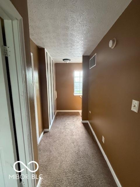 hall featuring visible vents, carpet flooring, a textured ceiling, and baseboards