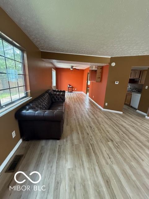 living area with visible vents, light wood-style flooring, a textured ceiling, and baseboards