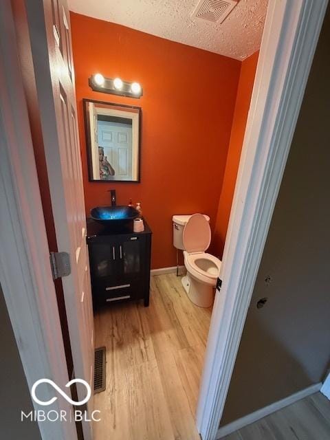 half bath featuring vanity, toilet, wood finished floors, and visible vents